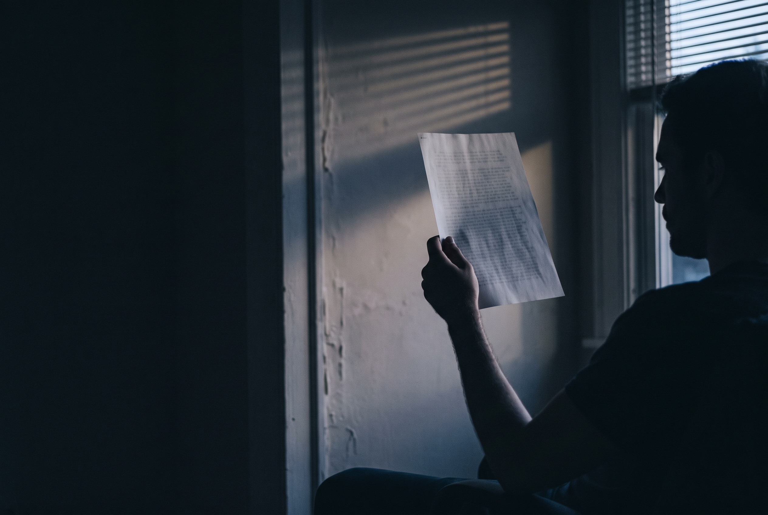 A single sheet of paper held up to a window at dusk, the print unreadable against the light.