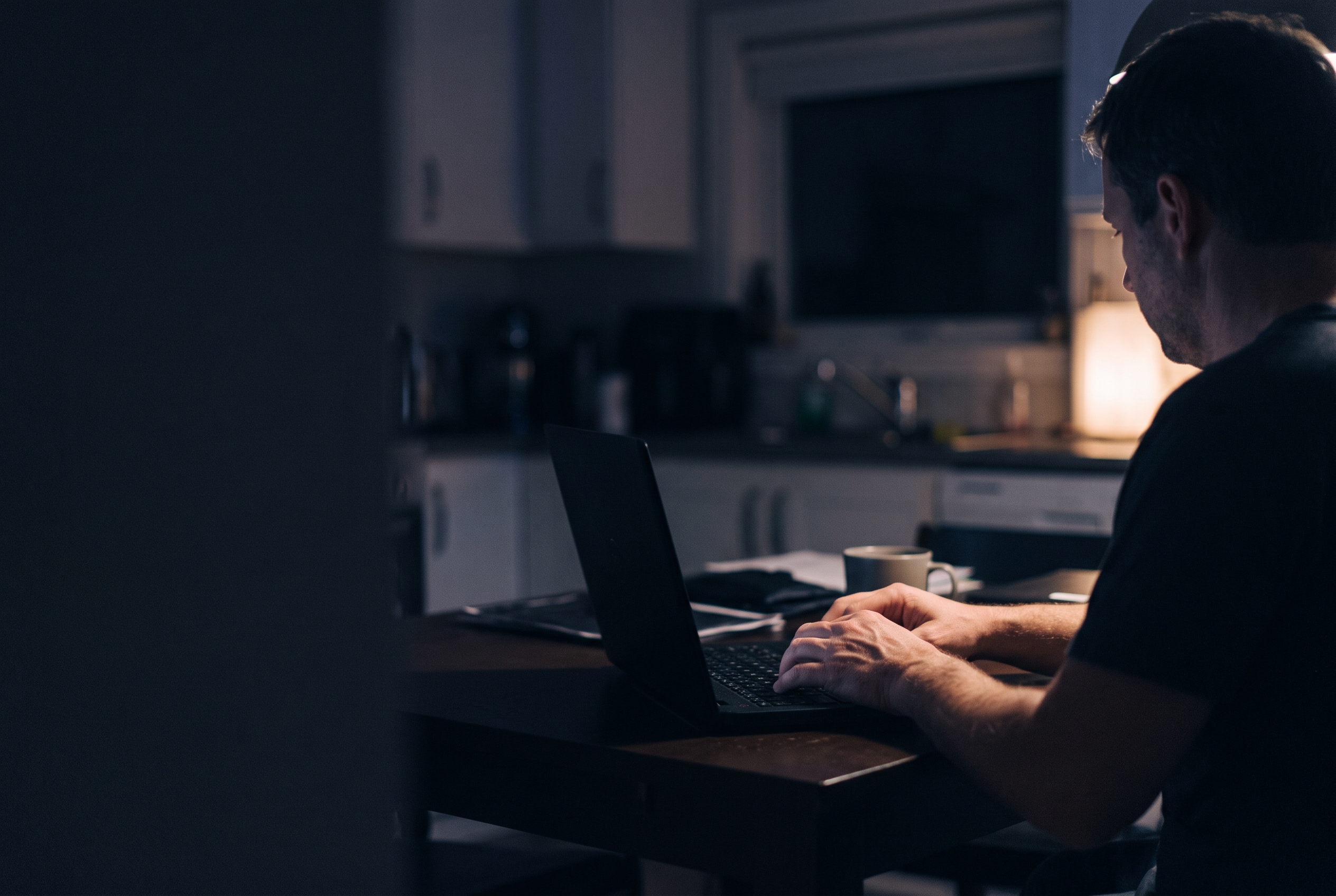 Hands on a laptop keyboard at a kitchen table at night.